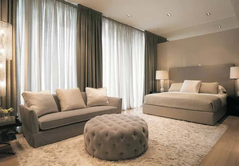 Photograph from the developer’s brochure: a bedroom suite with a sofa and a round tufted ottoman beside the bed, under full-length sheer curtains