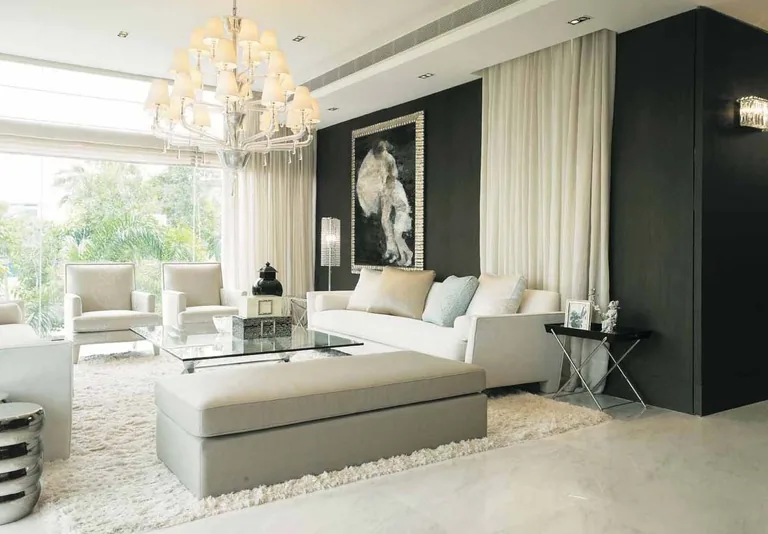 Photograph from the developer’s brochure: a living room in pale stone and cream with a chandelier, a low sofa and tall curtained windows
